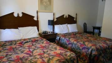 A hotel room with two single beds, each with a floral bedspread, a wooden headboard, a bedside table with a lamp, and a framed picture on the wall.