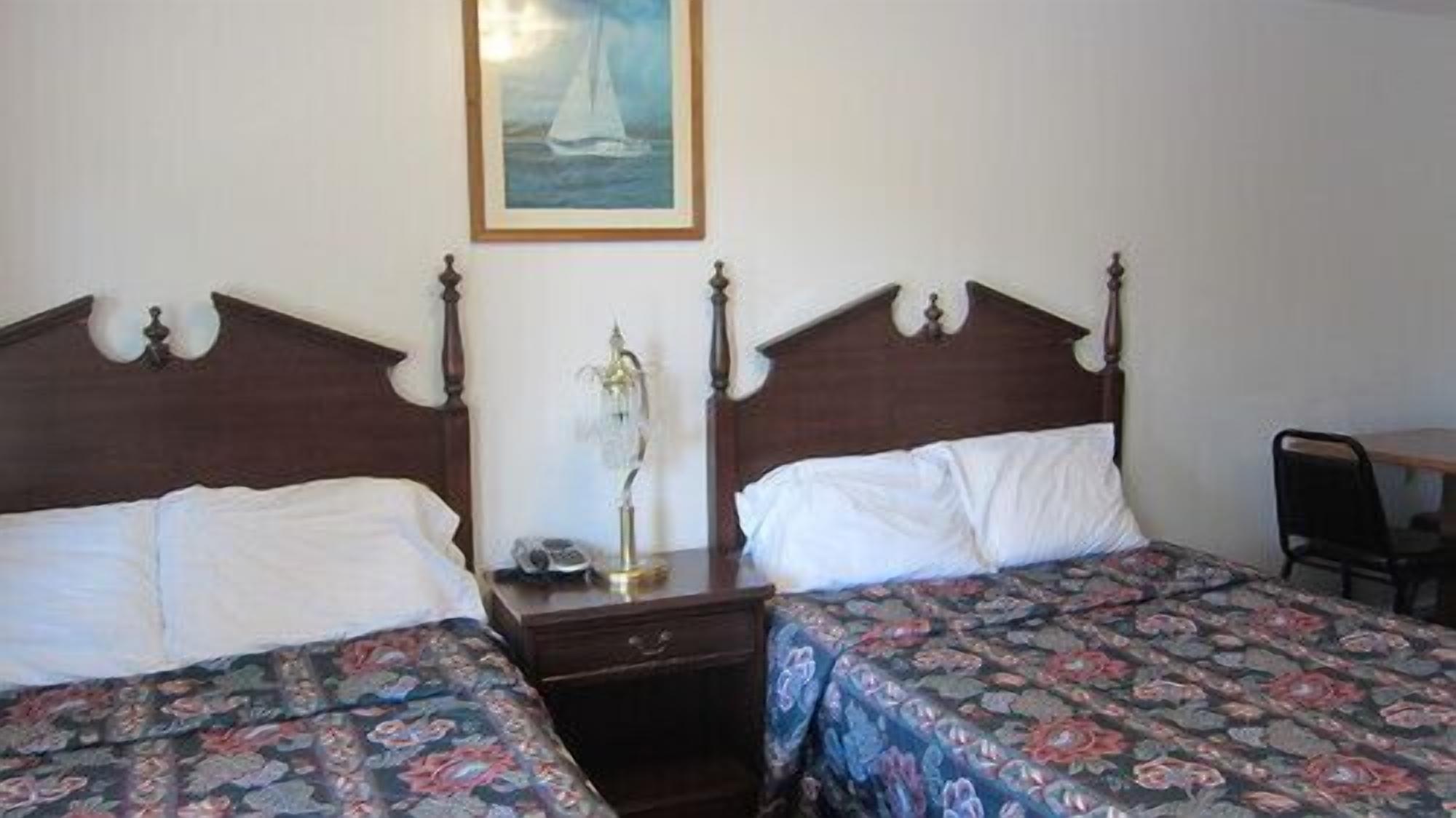 A room with two single beds, a nightstand with a lamp, and a painting on the wall.