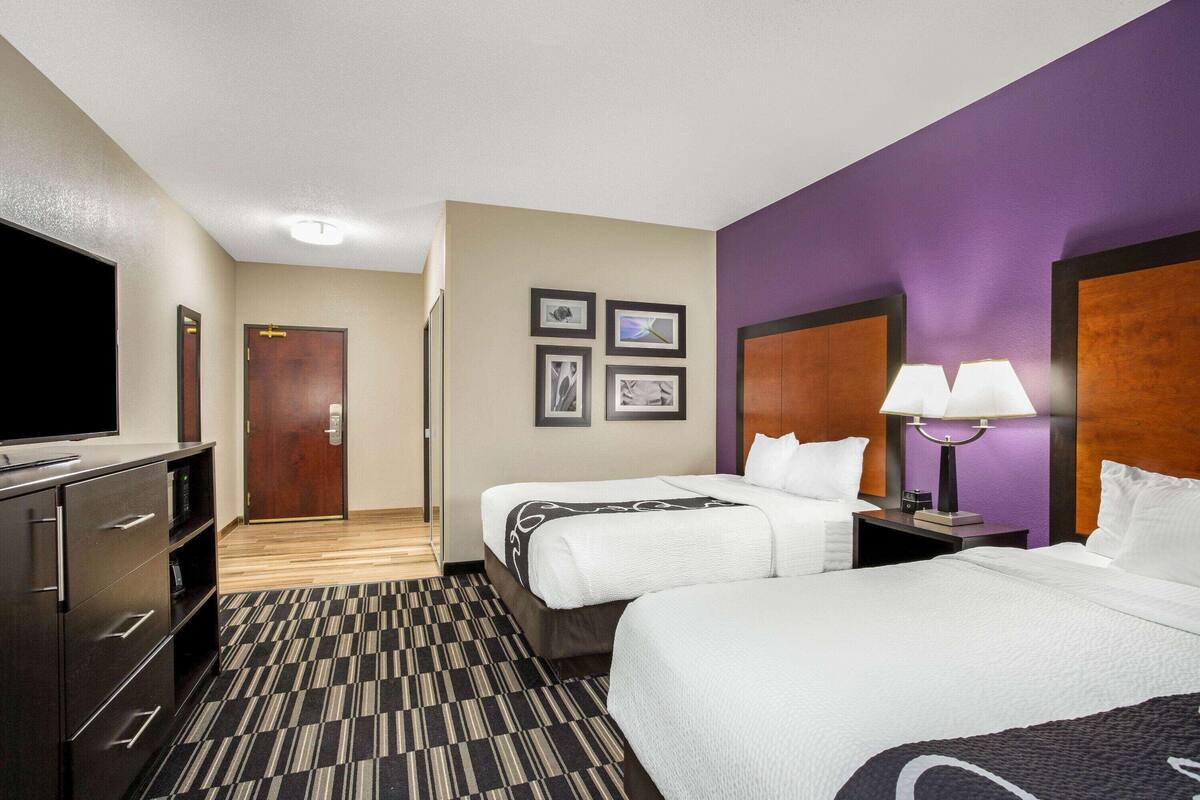 Ein Hotelzimmer mit zwei Betten, einem Fernseher, einem Schreibtisch und einer Lampe.