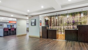 A modern reception area with a wooden floor, a reception desk, and a wall with a forest mural. - La Quinta Inn & Suites by Wyndham Norwich-Plainfield-Casino (Plainfield)