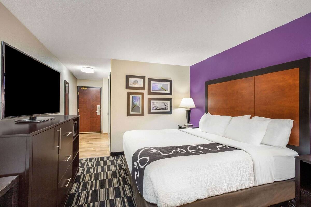 Ein Hotelzimmer mit einem Bett, einem Fernseher, einem Schreibtisch, einer Lampe und gerahmten Bildern an der Wand.