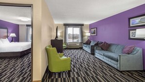 A hotel room with a bed, a green armchair, a grey sofa, and a purple wall. - La Quinta Inn & Suites by Wyndham Norwich-Plainfield-Casino (Plainfield)