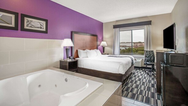 A hotel room with a large bed, a separate bed, a bathtub, a desk with a TV, and a window with a city view. - La Quinta Inn & Suites by Wyndham Norwich-Plainfield-Casino (Plainfield)