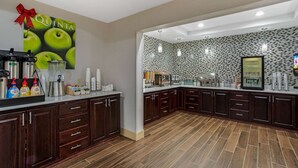 A modern kitchen with dark wooden cabinets, a tiled backsplash, and a large poster of green apples with a red bow. - La Quinta Inn & Suites by Wyndham Norwich-Plainfield-Casino (Plainfield)