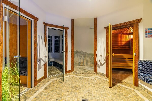 Un área de spa con suelo de mosaico, puertas de madera y una zona de estar con cojín estampado.