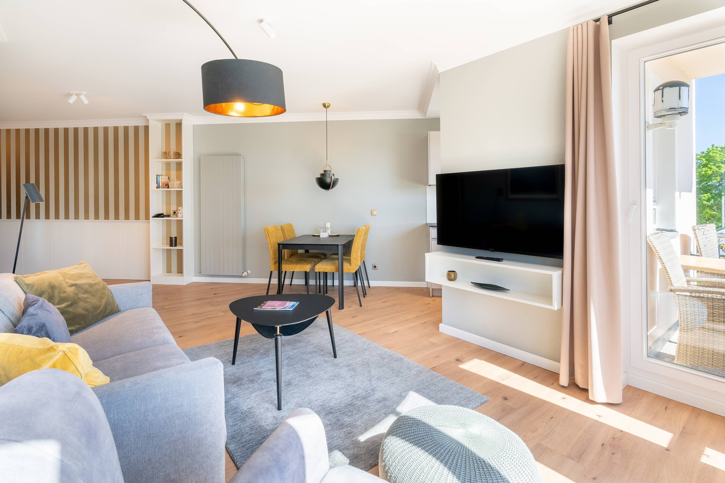 A modern living room with a sofa, a coffee table, a TV, and a dining area with yellow chairs.