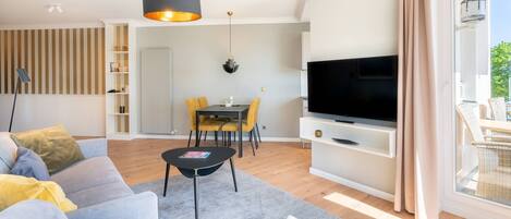 A modern living room with a sofa, a coffee table, a TV, and a dining area with yellow chairs.