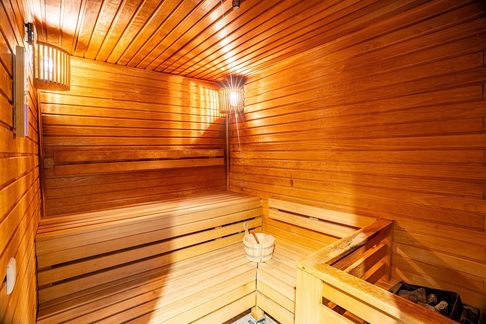 A wooden sauna with benches, a bucket, and a heater.