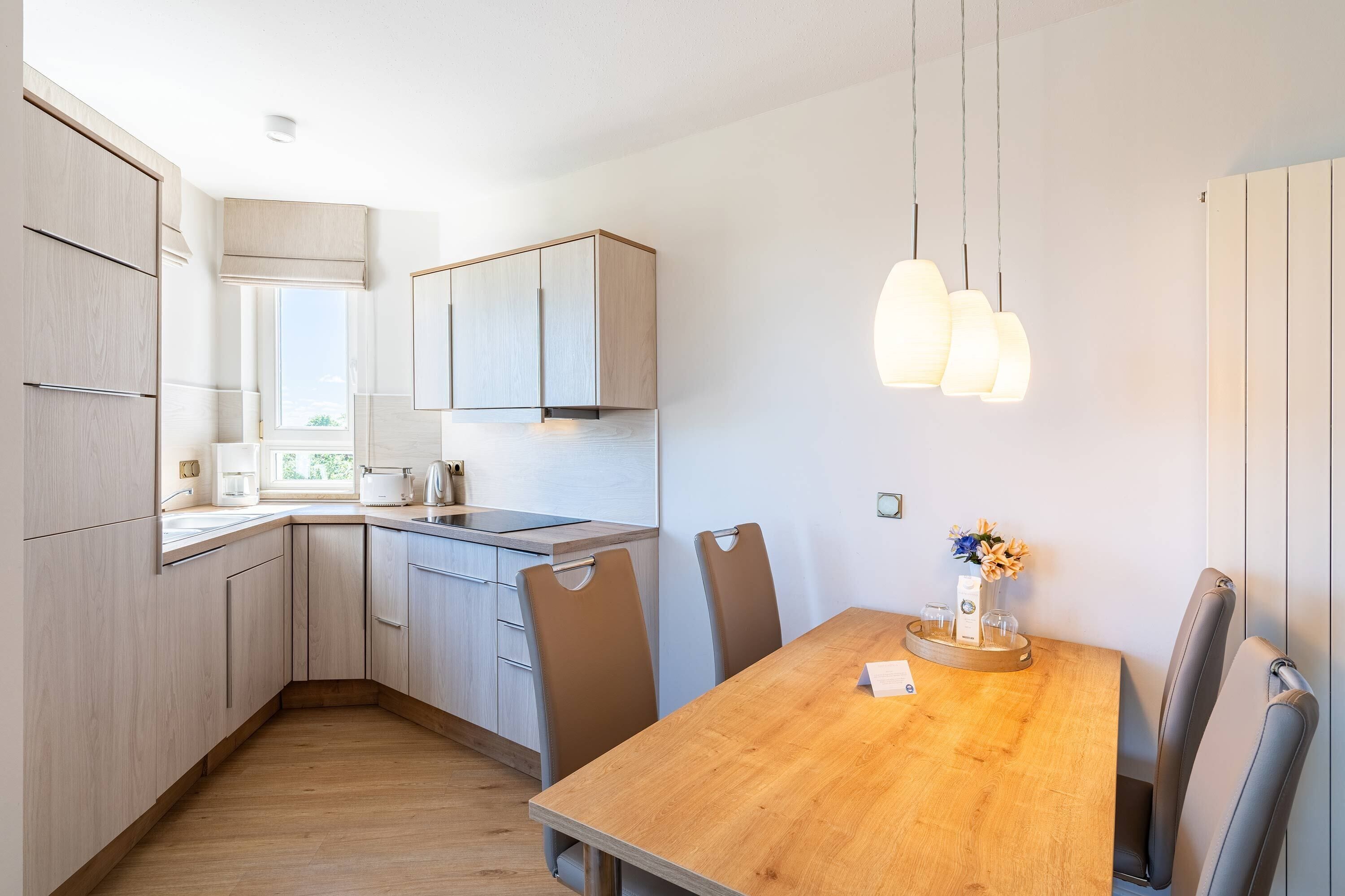 Una cocina moderna con armarios de madera, una mesa de comedor con sillas e iluminación colgante.