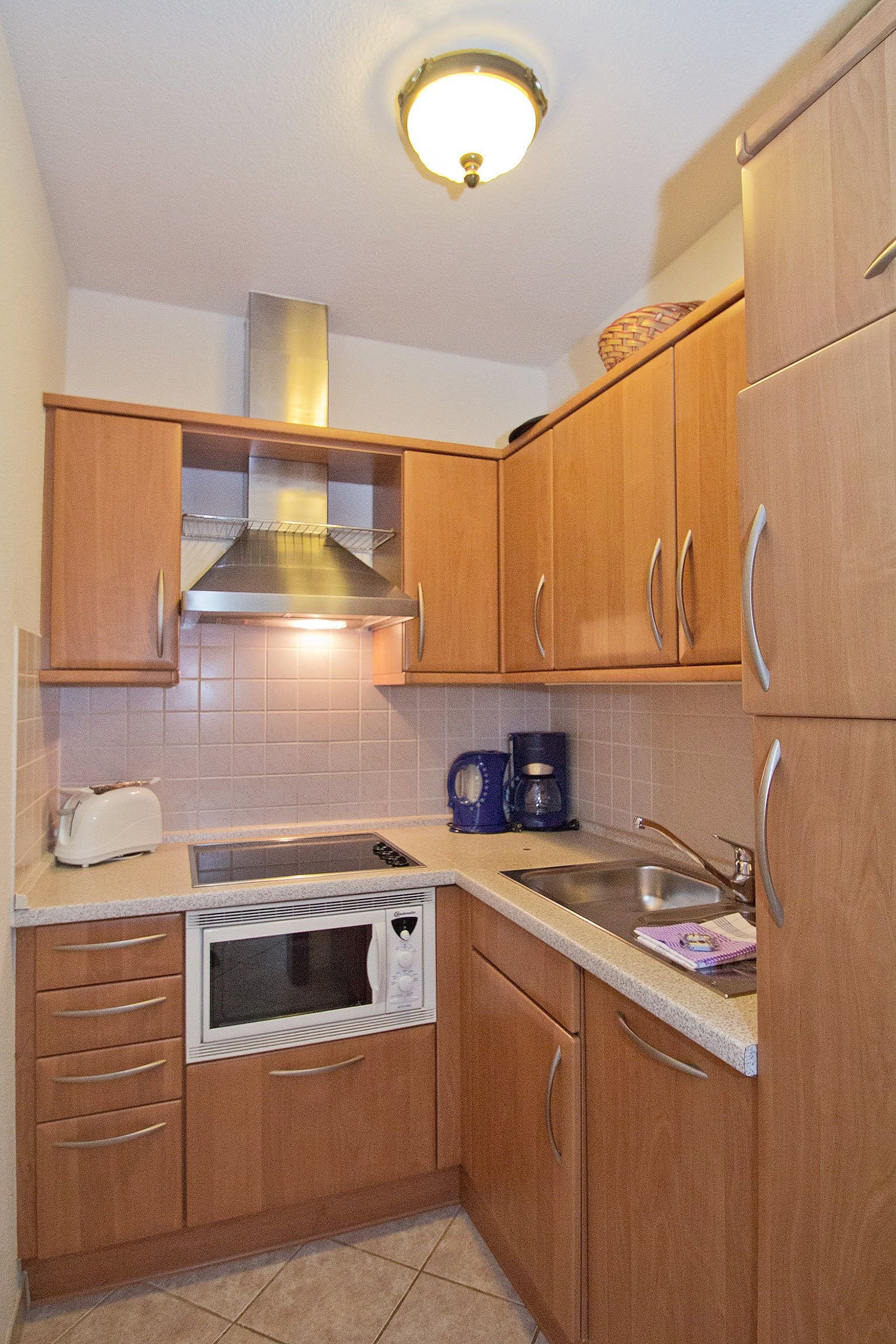 A compact kitchen with wooden cabinets, a stainless steel range hood, a microwave, a toaster, and a coffee maker.