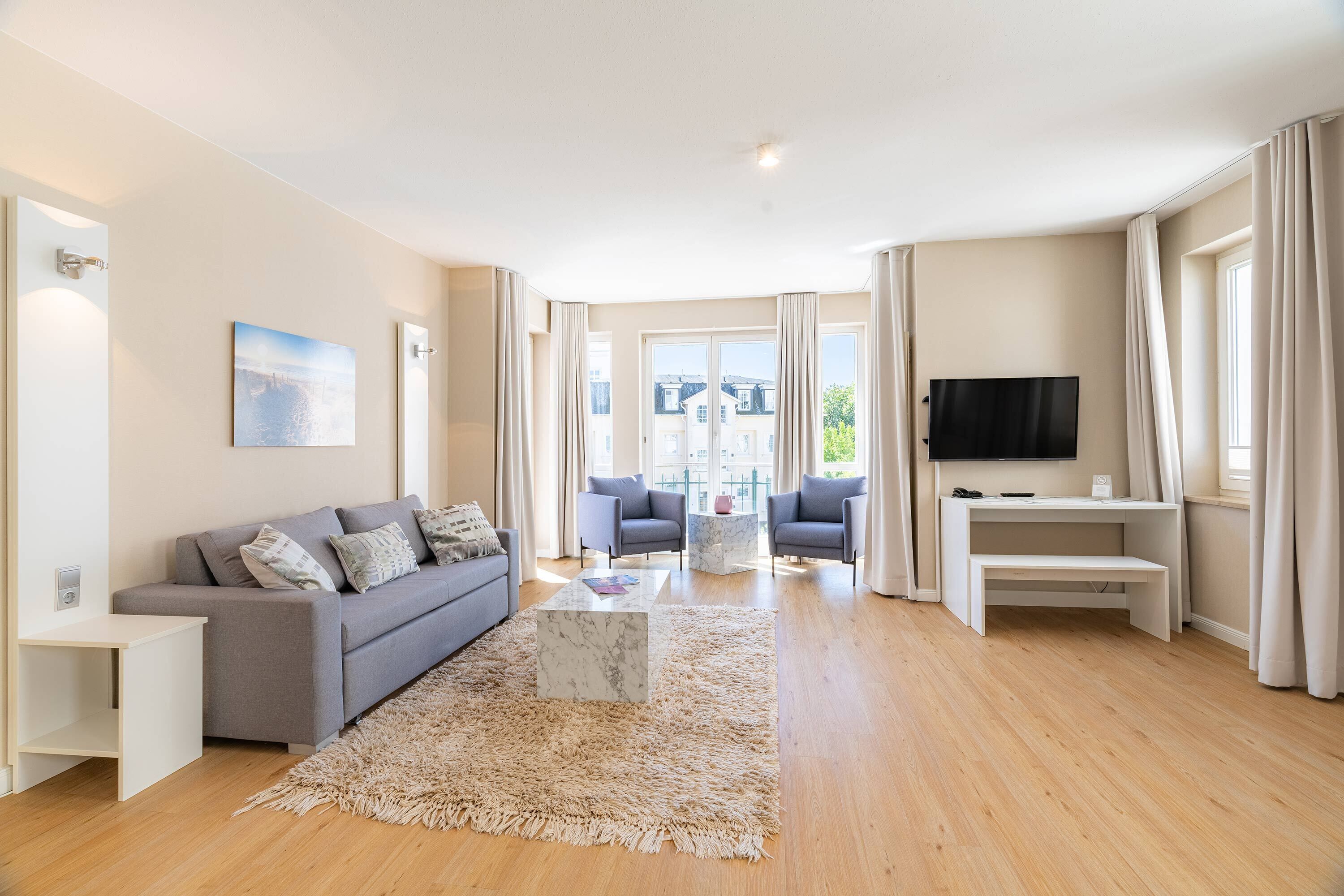 A modern living room with a sofa, coffee table, TV, and large windows.