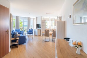A modern hotel room with a living area, dining space, and a view of the sea.