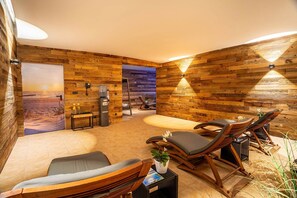 Ein Zimmer mit Holzwänden, einem Sofa, zwei Lounge-Sesseln, einem kleinen Tisch mit Pflanze und einem an der Wand befestigten Telefon.