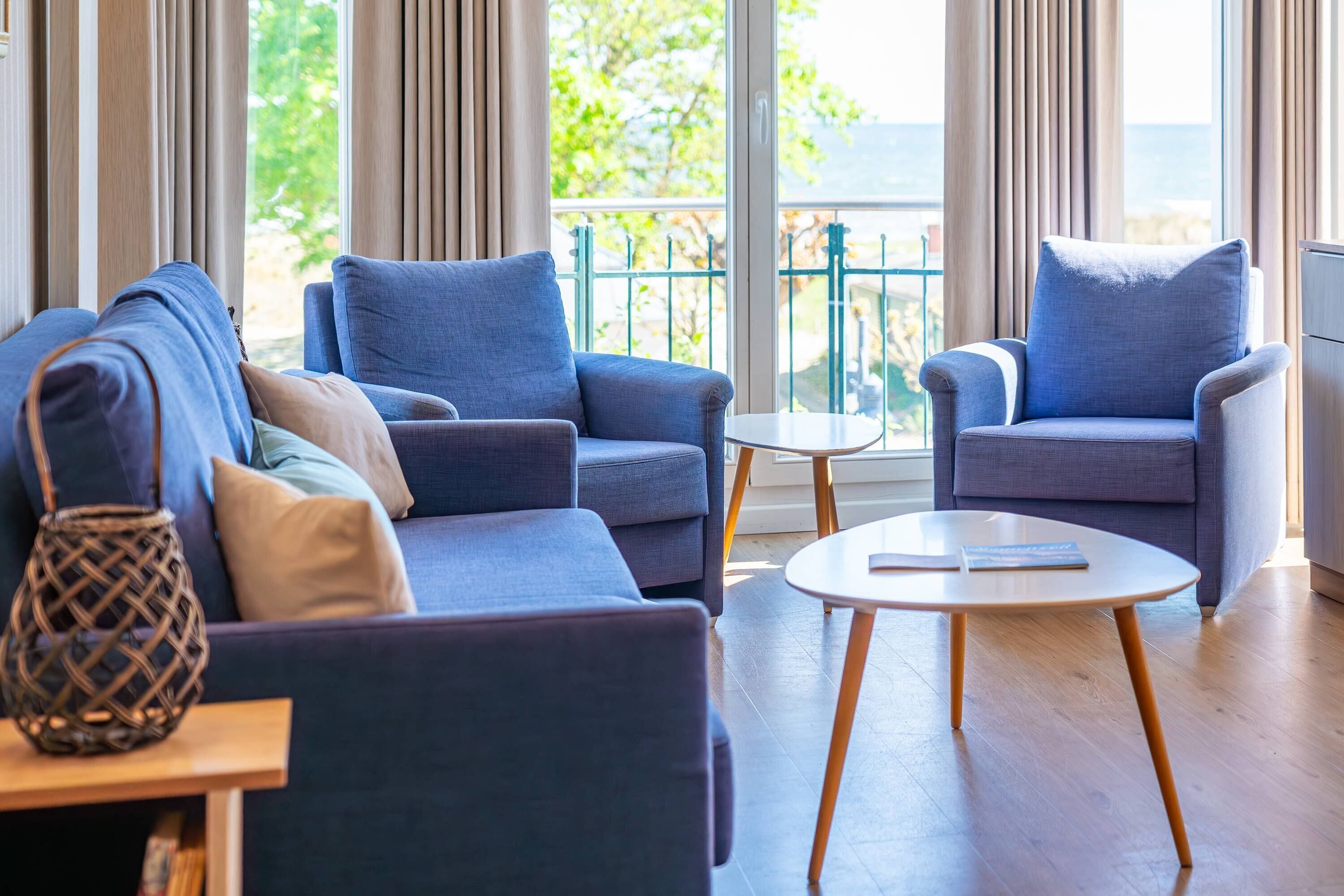 A modern living room with a sofa, armchairs, a small table, and a view of the outdoors.
