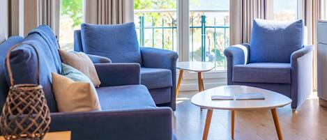A modern living room with a sofa, armchairs, a small table, and a view of the outdoors.