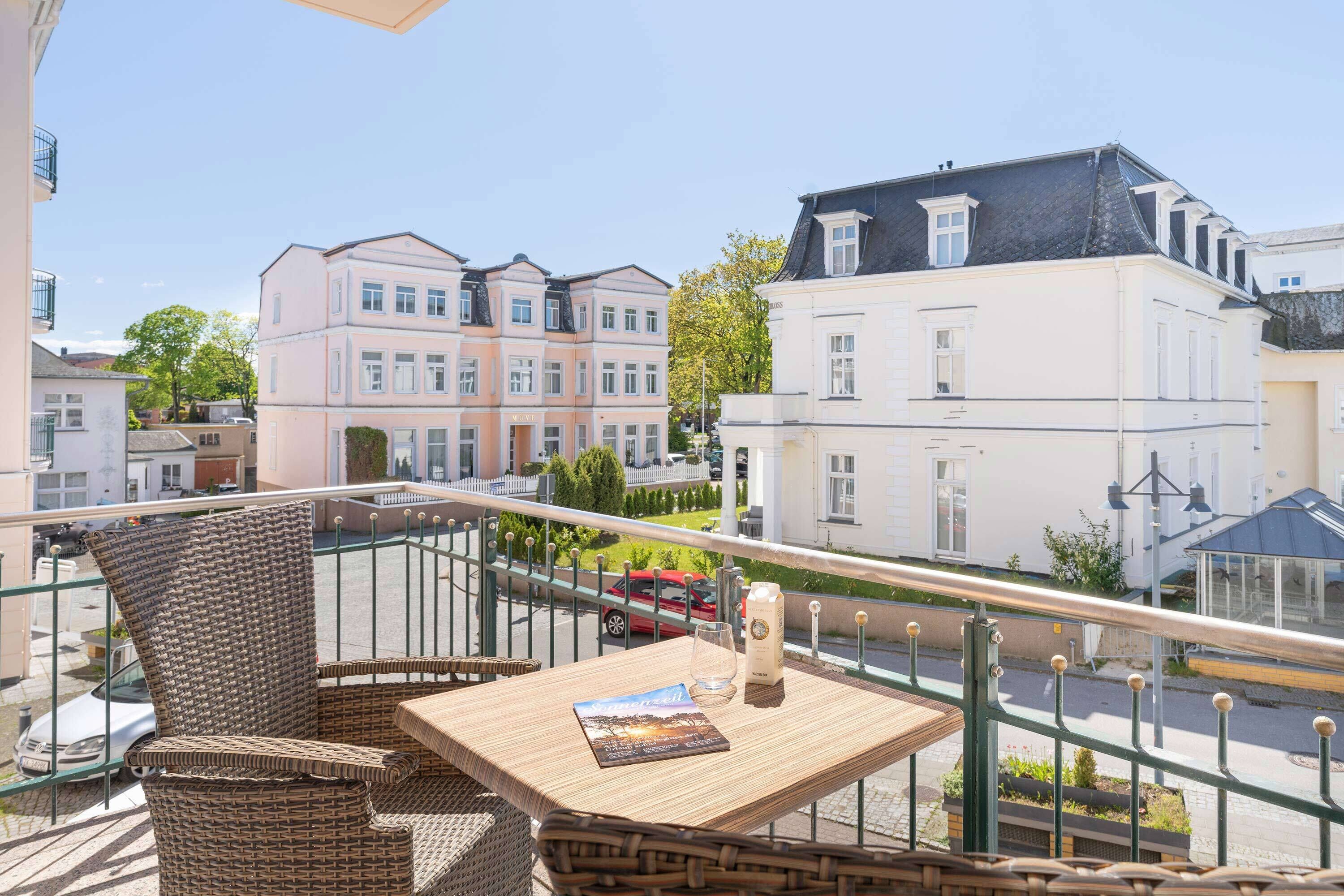 A balcony with wicker furniture, a table with a book and a bottle, and a view of buildings.