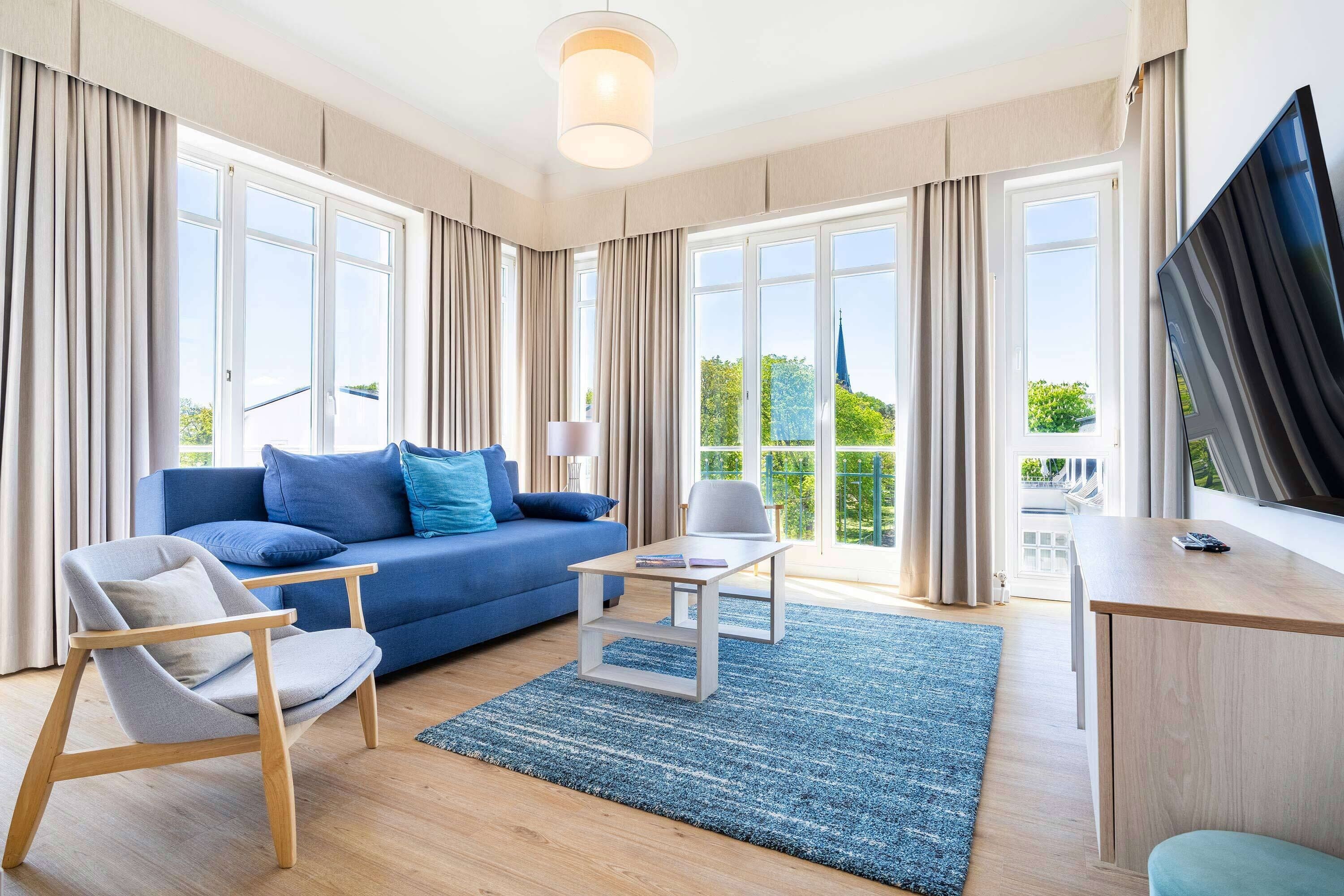 Een moderne woonkamer met een blauwe bank, een houten stoel, een kleine tafel en een televisie.