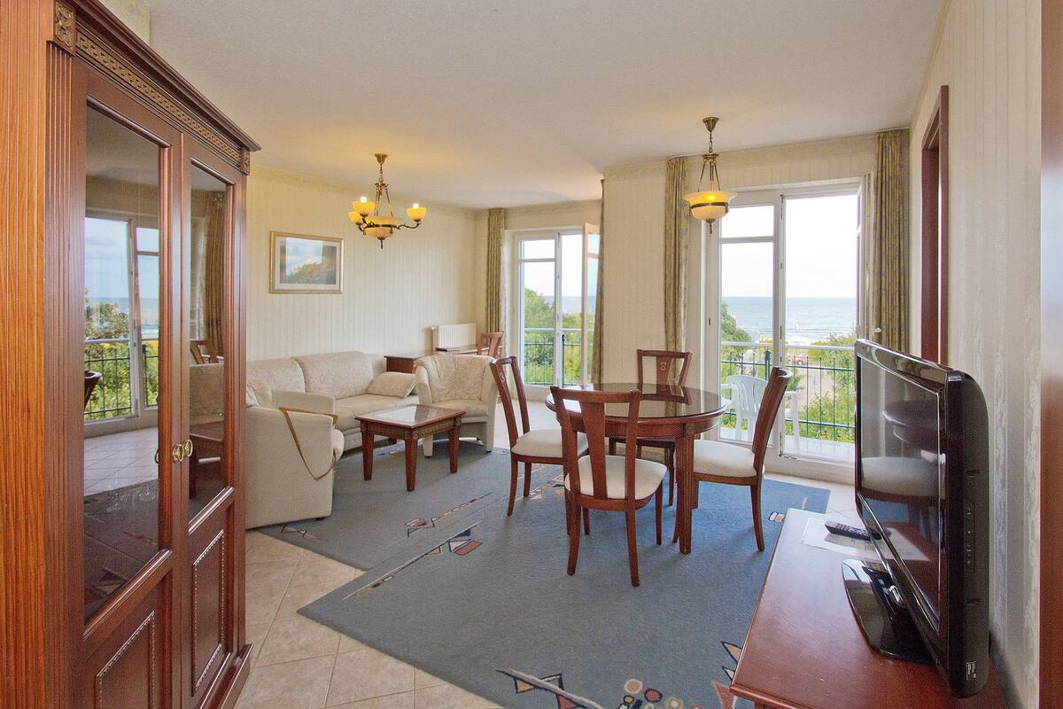 A spacious living area with a sofa, dining table, chairs, and a television.