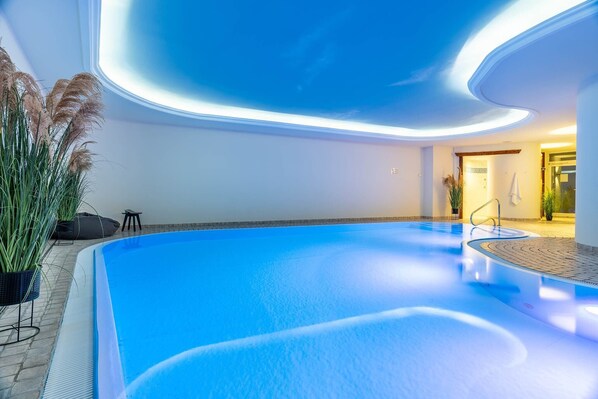 An indoor swimming pool with a curved ceiling and a view of the adjacent room. - SEETELHOTEL Ostseeresidenz Ahlbeck (Heringsdorf)