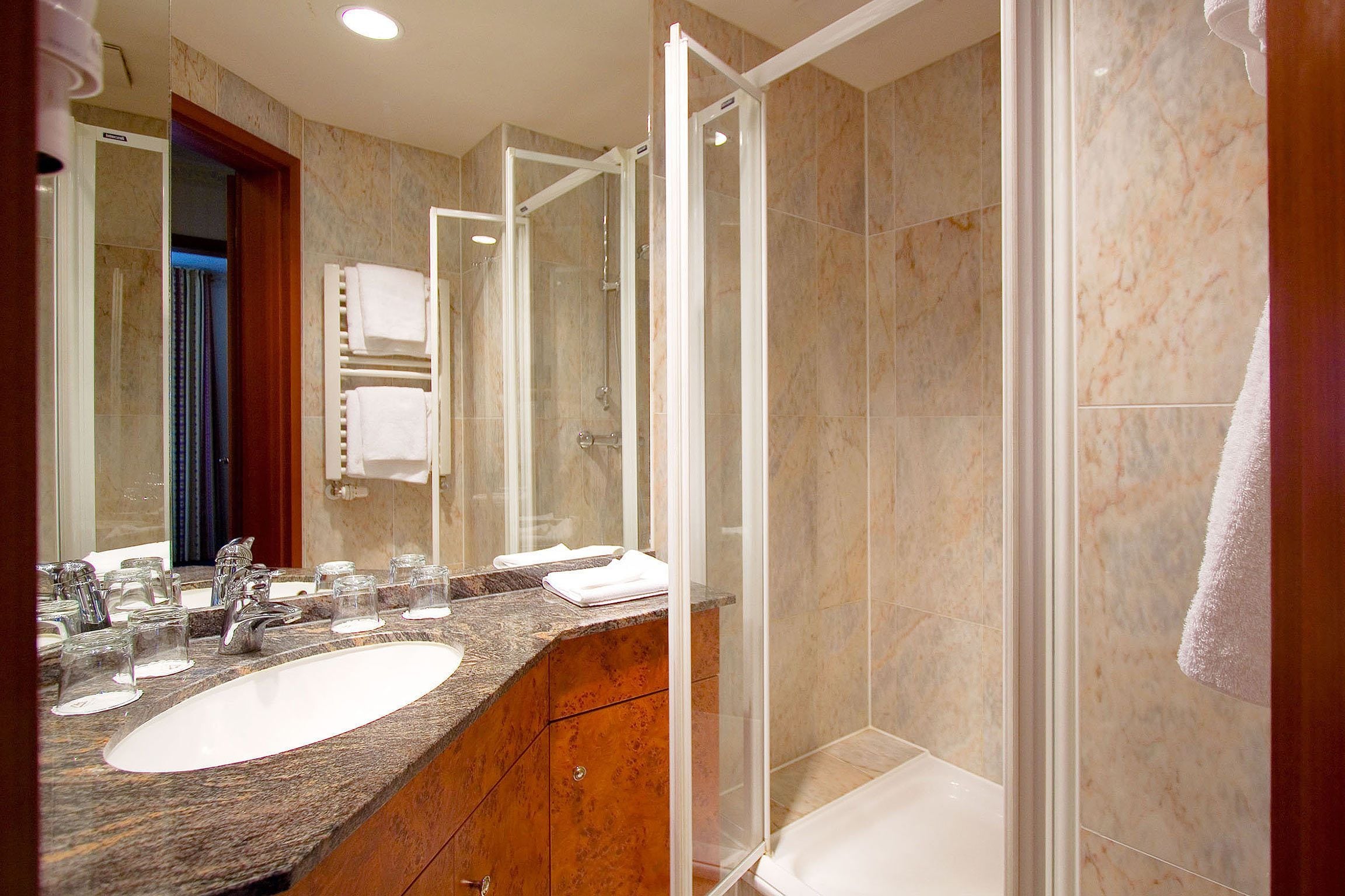 A modern bathroom with a marble sink, glass shower enclosure, and a wooden vanity.