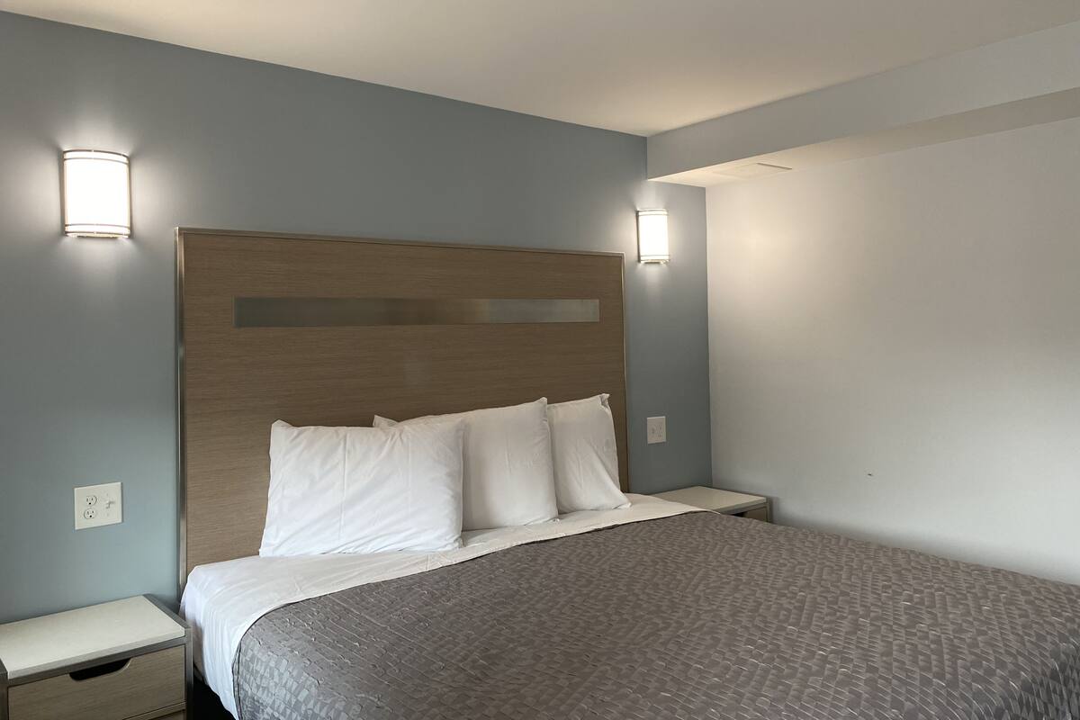 Una cama bien hecha con cabecera de madera, dos mesitas de noche e iluminación en la pared.