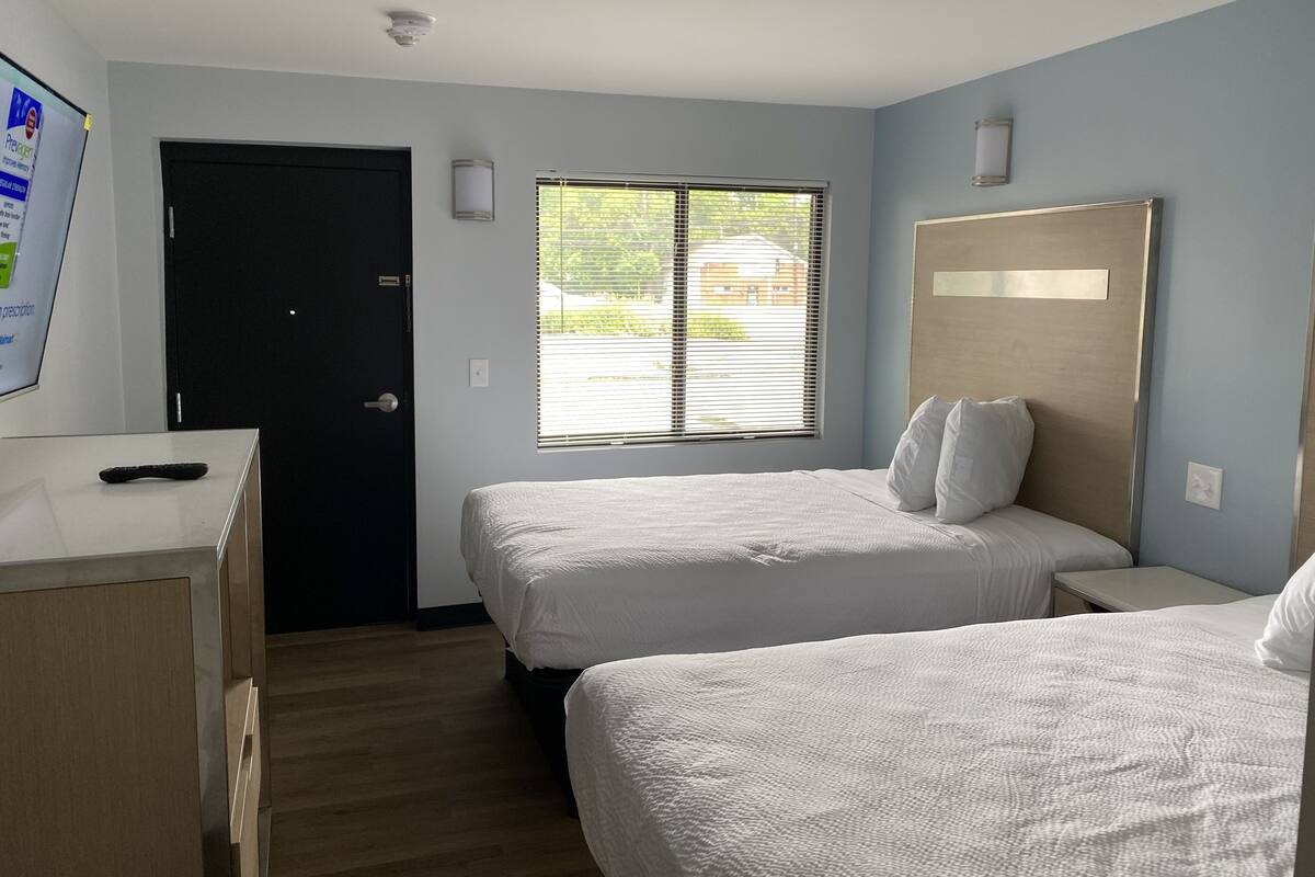 Habitación de hotel con dos camas, un escritorio, una puerta negra y una ventana con persianas.