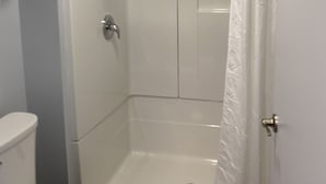 A shower stall with a white shower curtain, a toilet, and a towel rack.