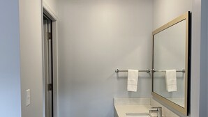 A modern bathroom with a white sink, a large mirror, and a towel rack.