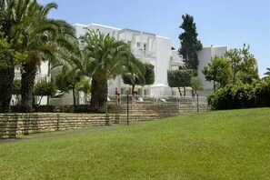 A hotel with a white facade, palm trees, and a stone wall.