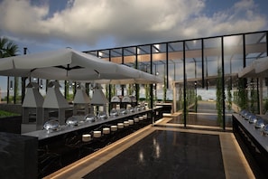 A modern outdoor dining area with a long counter, multiple umbrellas, and a glass-enclosed space.