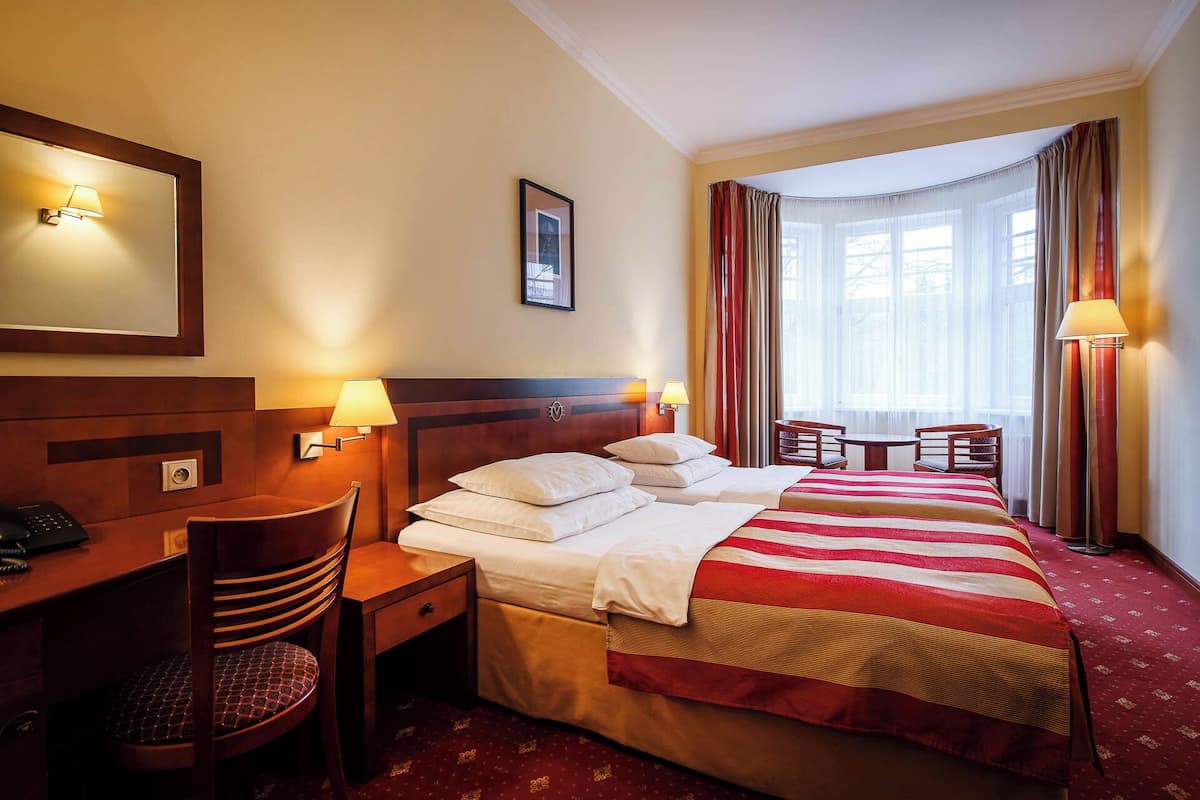 A hotel room with a bed, desk, chair, and a window with curtains.