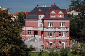 A multi-story building with a prominent entrance, a staircase leading to the main door, and a small outdoor seating area with tables and chairs. - Hotel Villa (Prague)