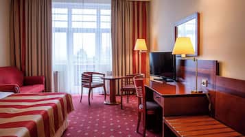 Una habitación de hotel con cama, escritorio, televisor, sillón y lámpara.