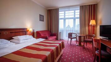 Ein Hotelzimmer mit Bett, Schreibtisch, Stuhl, Fernseher und einem Vorhangfenster.
