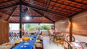 A spacious dining area with a high ceiling and large windows, featuring a long table set for a meal, surrounded by chairs. - Pousada Bahia Inn (Cairu)
