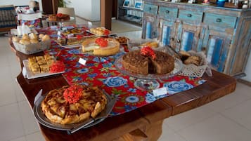 Una mesa de buffet con diversos postres y pasteles, un mueble de madera con electrodomésticos de cocina, y un mantel con motivos florales.
