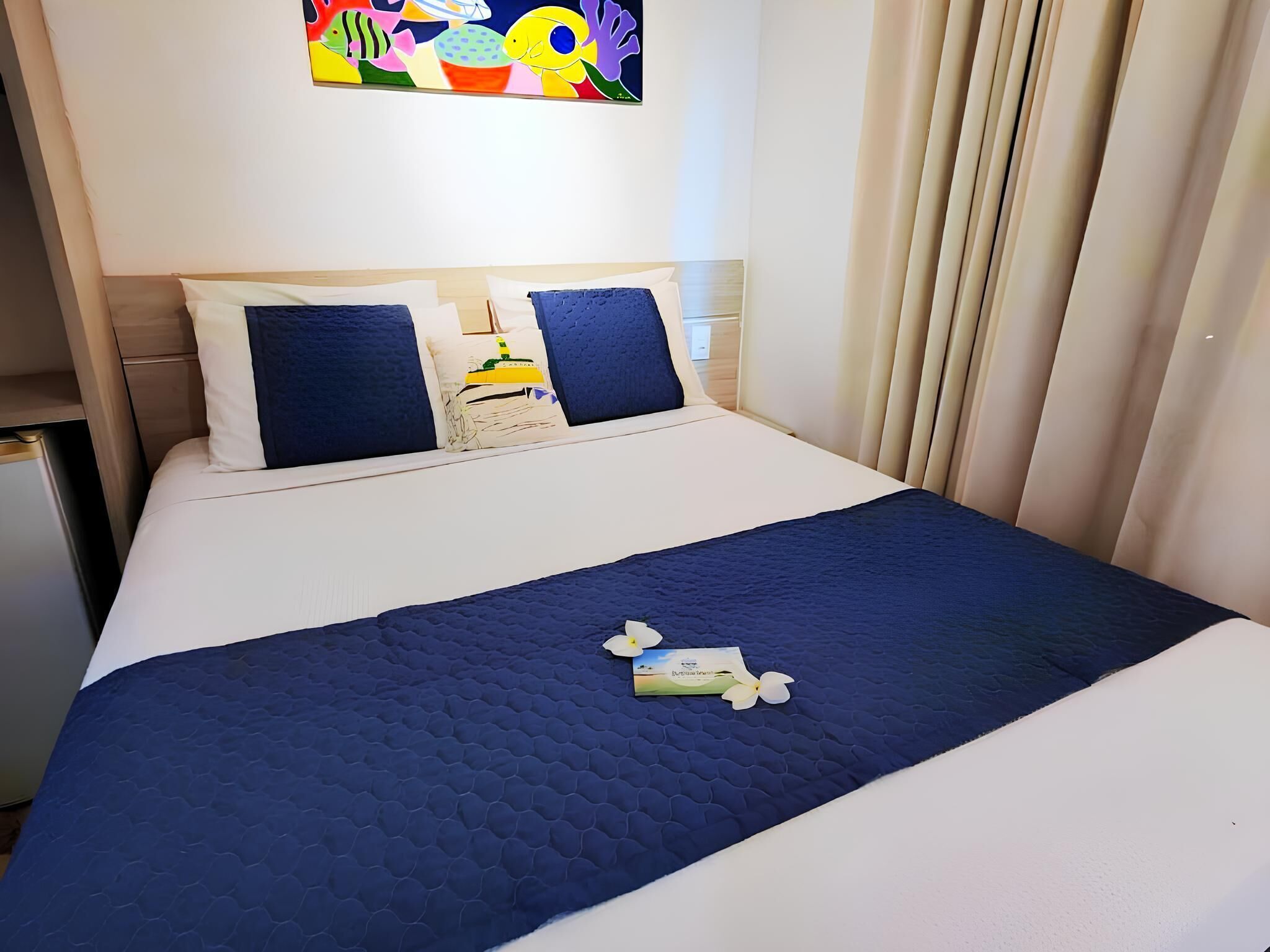 A hotel room with a bed, pillows, a nightstand, and a painting on the wall.