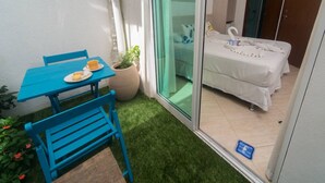 A small balcony with a blue table and chairs, a potted plant, and a bed with white bedding and a swan decoration. - Pousada Bahia Inn (Cairu)