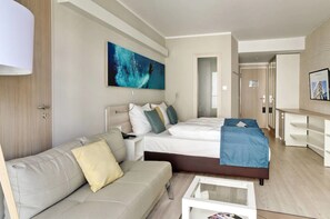 Quarto de hotel moderno com uma cama grande, um sofá, uma mesa de centro e um quadro na parede.