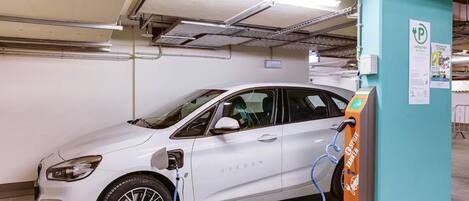 A white electric vehicle charging at a station in a parking garage.