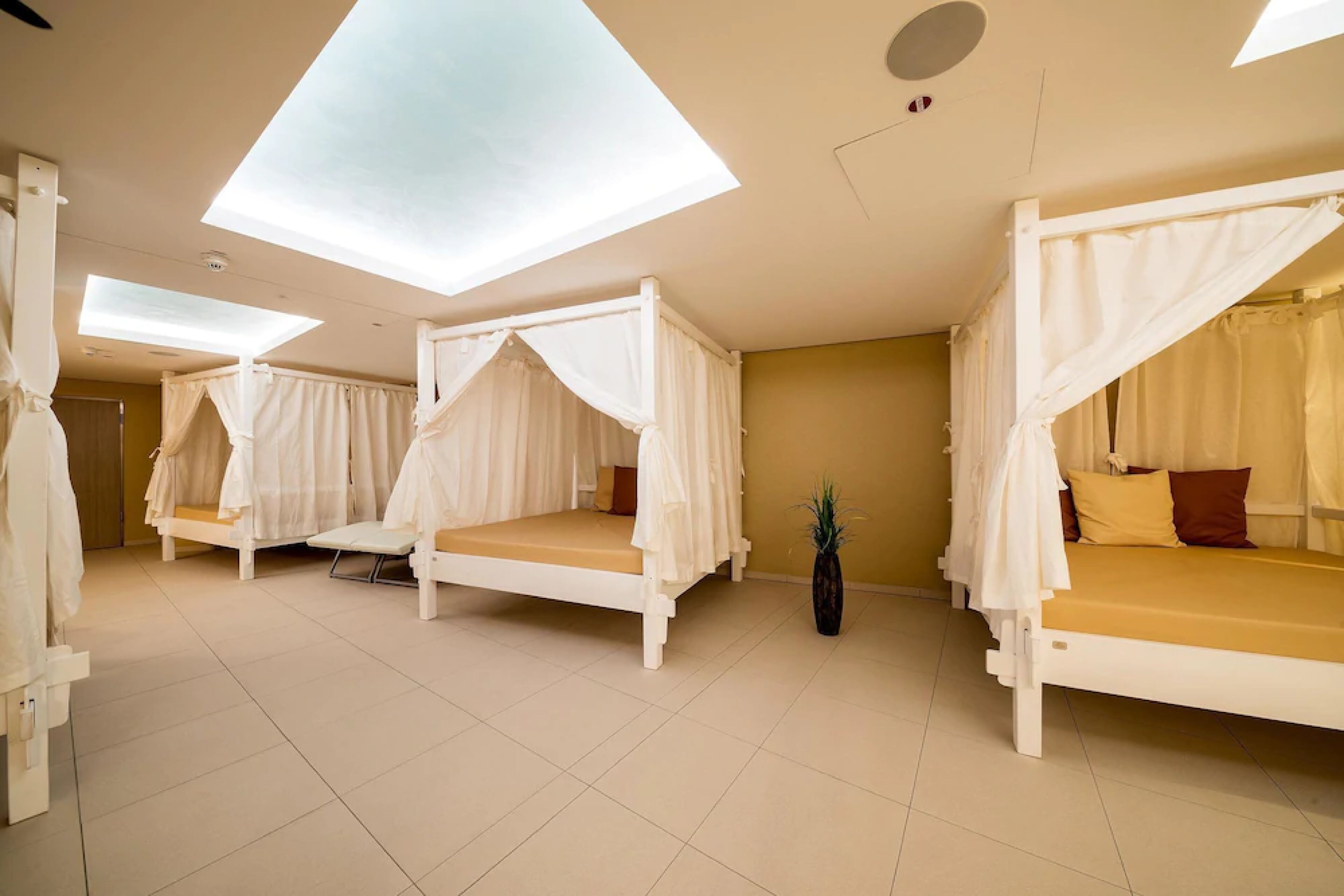 Une chambre avec quatre lits, chacun doté d’un baldaquin, et une lucarne au plafond.