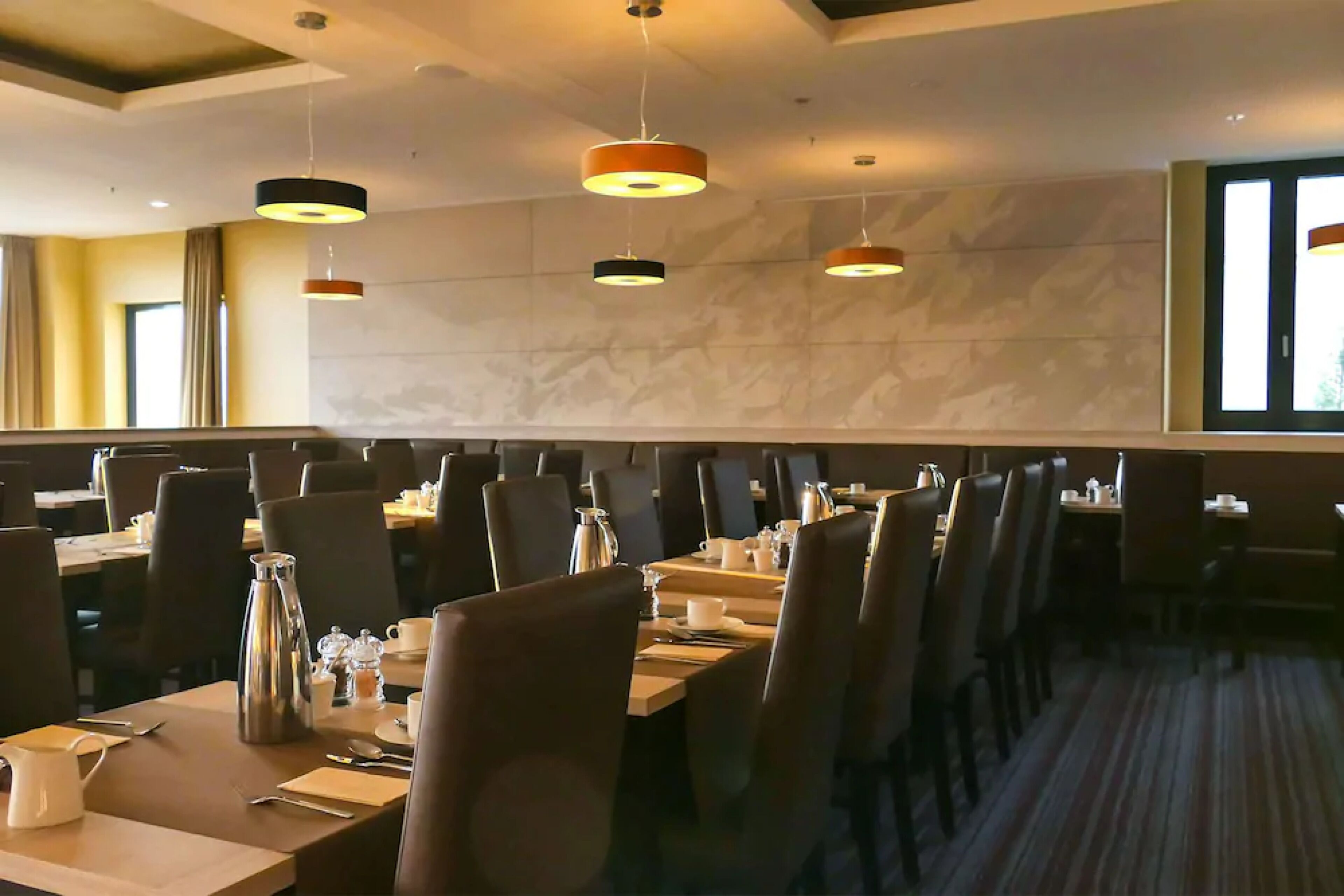 A hotel dining area with multiple tables, chairs, and hanging pendant lights.