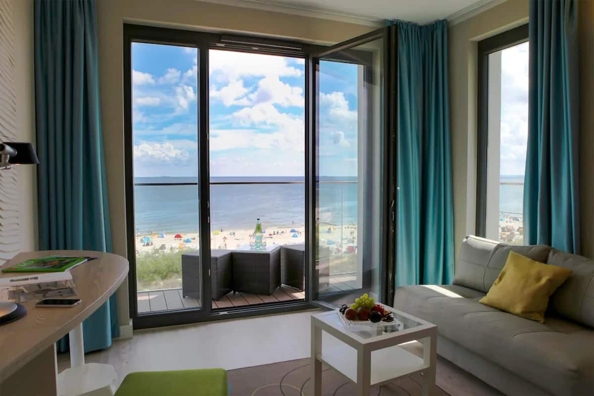 Una sala de estar moderna con un amplio ventanal corredizo que da a un balcón con vista al mar y la playa.