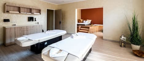 A modern hotel room with two massage tables, a wooden cabinet, and a small plant.