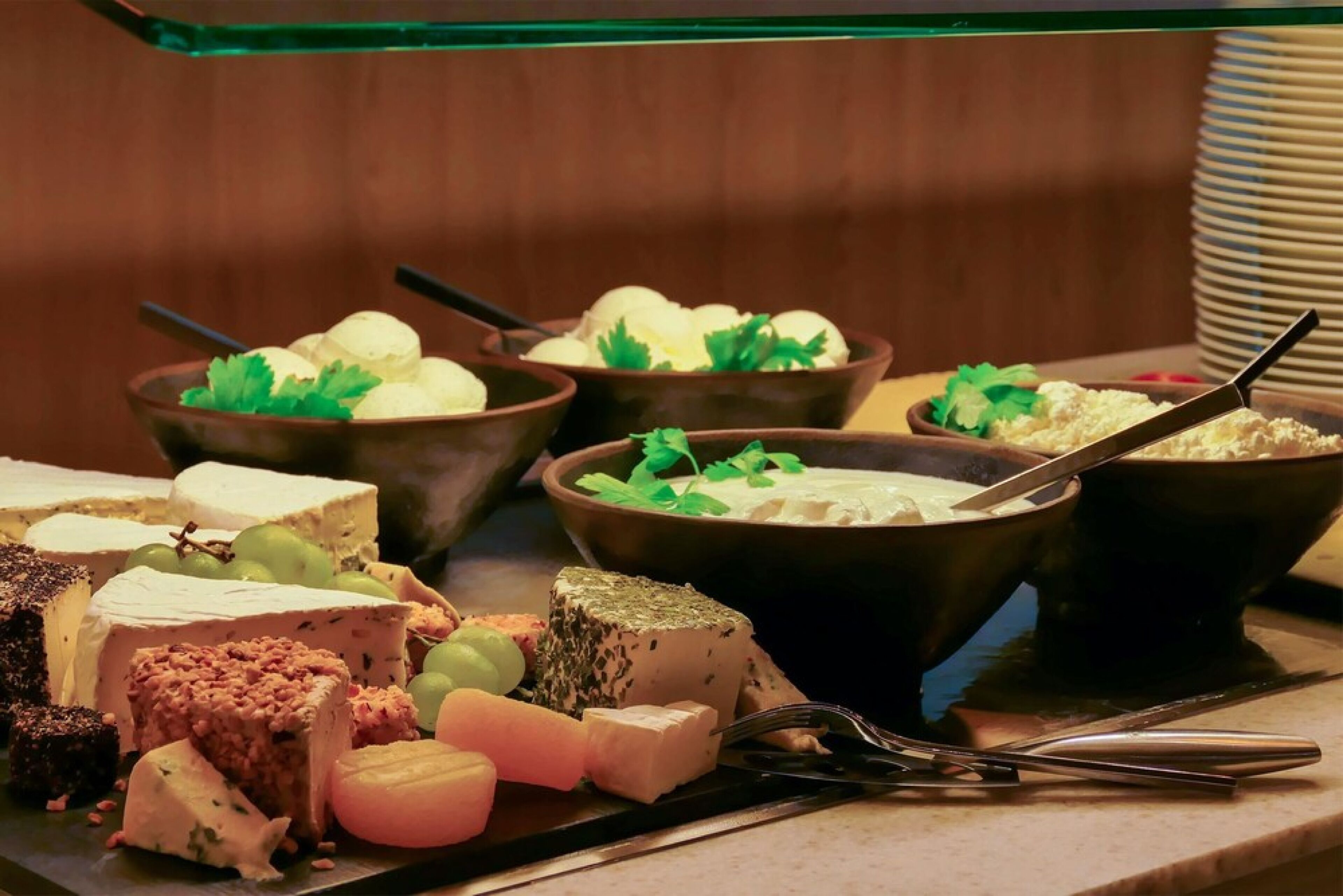 A variety of cheeses and fruits on a tray, with a fork and knife placed beside them.