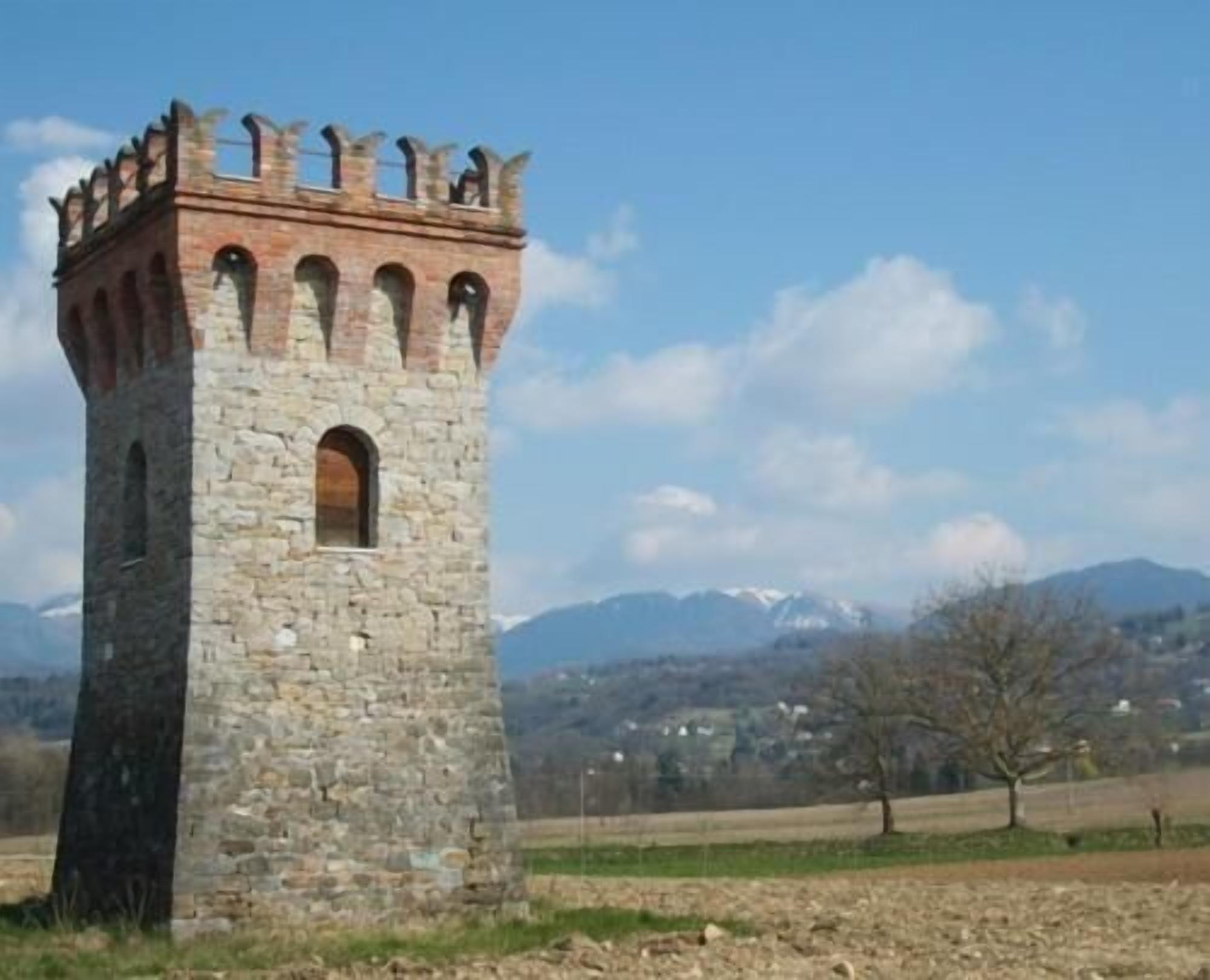 Una torre in pietra con finestre ad arco e merlature, sullo sfondo di montagne.