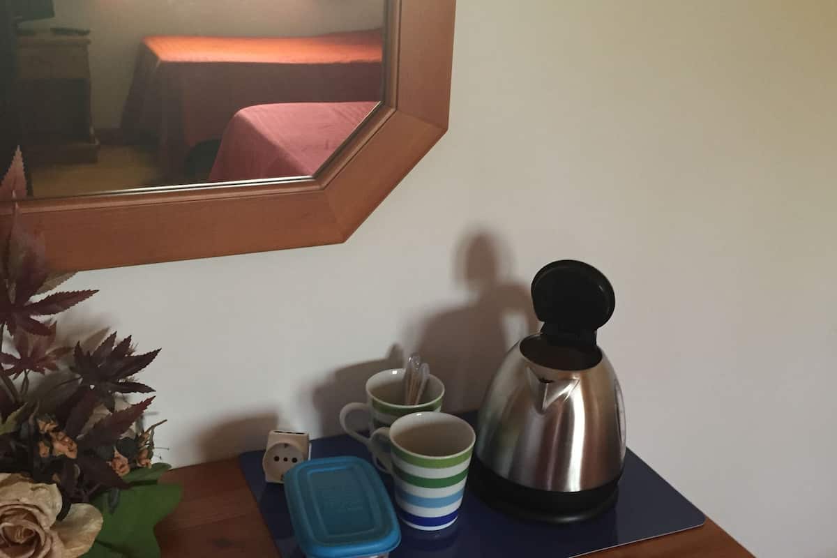 Uma cômoda de madeira com espelho, uma cafeteira, duas canecas listradas, um recipiente azul e uma planta em vaso.