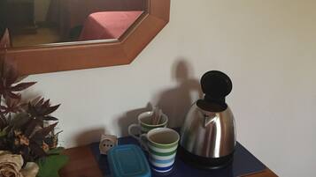 A wooden dresser with a mirror, a coffee maker, two striped mugs, a blue container, and a potted plant.