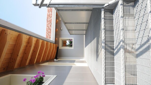 A modern building with a sloped roof, a wooden exterior wall, and a metal mesh fence. - Affittacamere Dormire Caldi (Borgo Valbelluna)