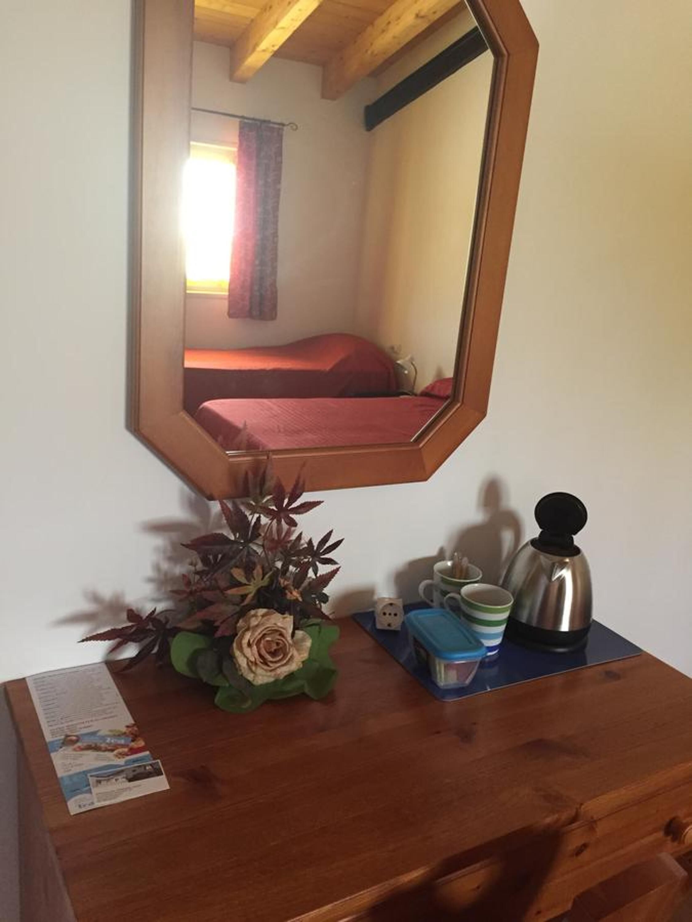 Ein hölzerner Kommode mit Spiegel, der ein Zimmer mit Bett und Fenster reflektiert.